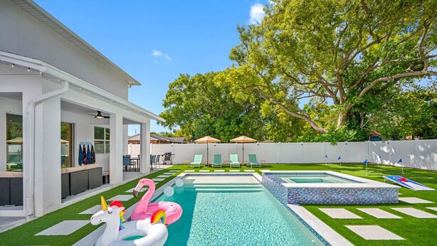 A backyard with a swimming pool, artificial flamingos, and a white house.
