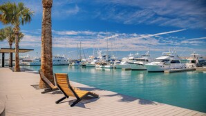 Un puerto deportivo con varios yates amarrados, una terraza de madera con una tumbona y palmeras.