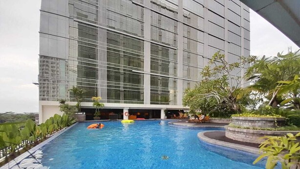 Una piscina con agua azul cristalina, rodeada por un edificio moderno con grandes ventanales.