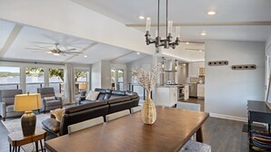 A spacious living area with a dark wood dining table, a black leather sofa, and a large window offering a view of the outdoors.