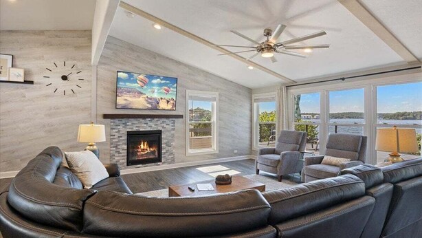 A living room with a fireplace, leather sofas, a ceiling fan, and large windows overlooking a scenic view.