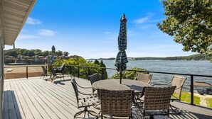 A wooden deck with wicker furniture and a table, overlooking a body of water with a clear sky.