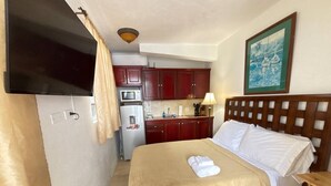 A compact hotel room with a bed, a small desk, a microwave, and a refrigerator. - Sleek & Sunny Island Studio | Kitchenette (St. Thomas)