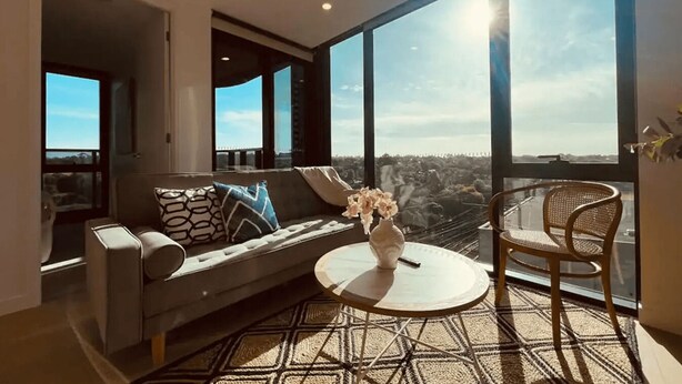 Un salon moderne comprenant un canapé, une table ronde et un fauteuil, avec de grandes fenêtres offrant une vue sur la ville.