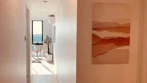 Un couloir donnant sur un balcon, avec une plante et une œuvre d’art abstraite accrochée au mur.