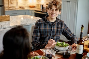 Iemand zit aan een eettafel met een saladekom en een fles wijn.