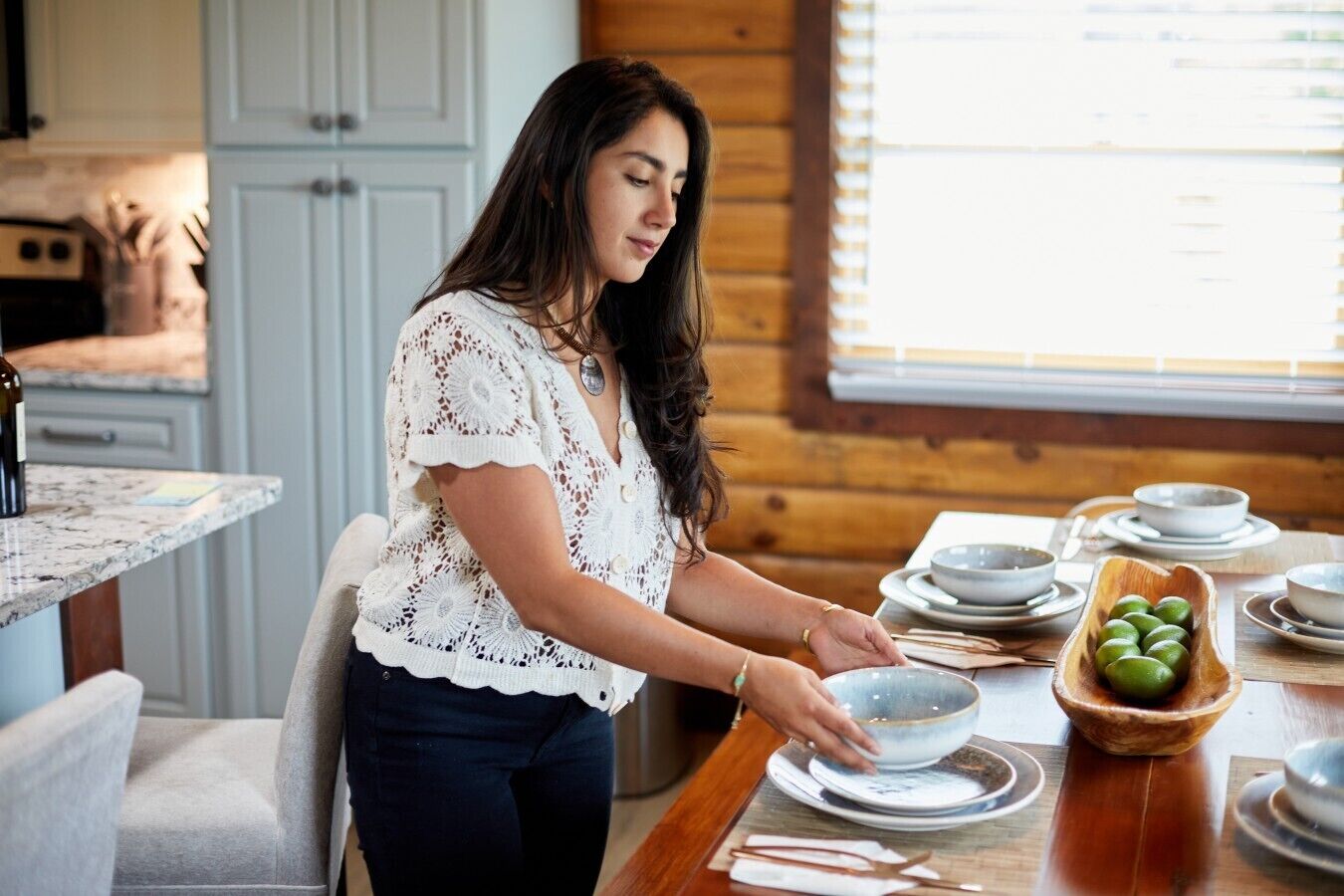 Une personne servant des plats à une table à manger en bois, avec des bols et des assiettes.
