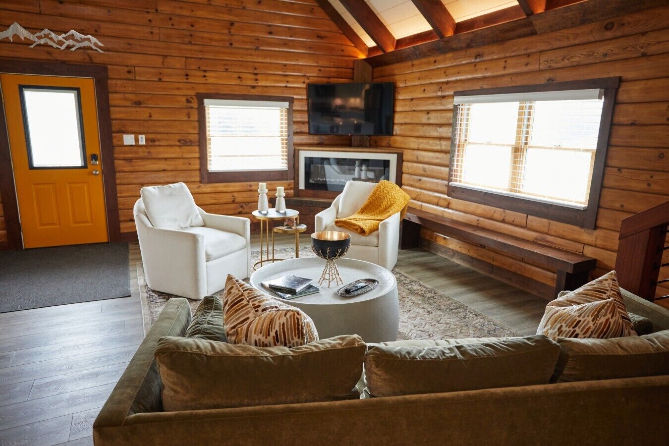 Een woonkamer in een blokhut met een bank, stoelen, een salontafel en een televisie.