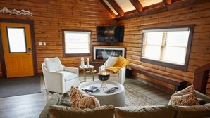 Ein rustikales Holzhaus-Interieur mit einer Couch, Sesseln, einem Couchtisch und einem Fernseher.