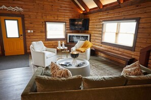 A log cabin interior with a sofa, chairs, a coffee table, and a television.