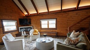Ein Blockhaus-Innenraum mit Kamin, Sitzecke und Fernseher.