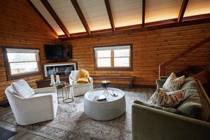 A log cabin interior with a fireplace, seating area, and a television.