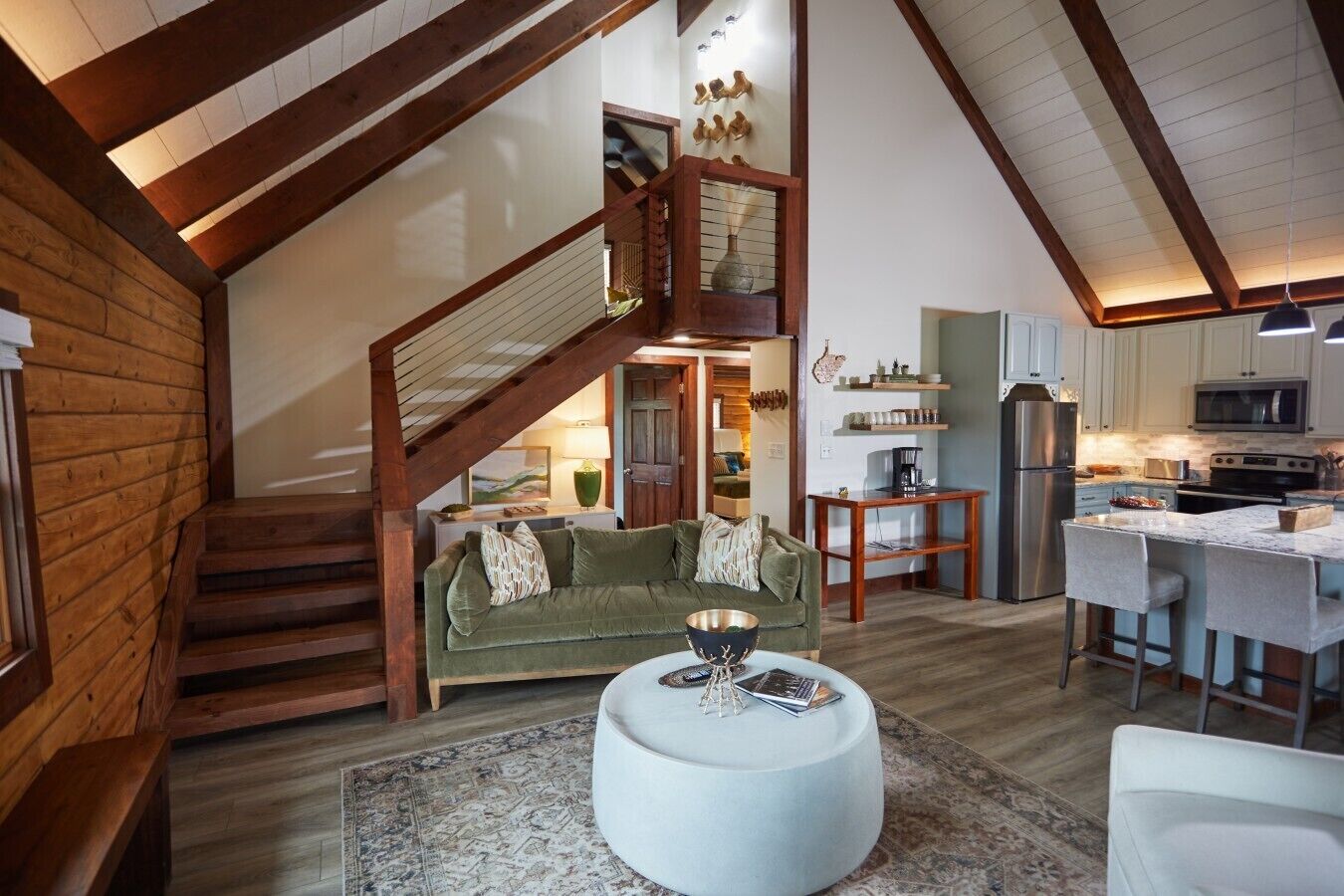 A spacious living area with a staircase, a green sofa, a round coffee table, and a kitchen with modern appliances.