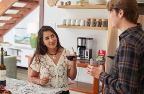 A person holding a wine glass in a room with a coffee maker and shelves with mugs.