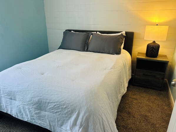 A neatly made bed with a white duvet and two pillows, a small bedside table with a lamp, and a wall with a textured pattern.