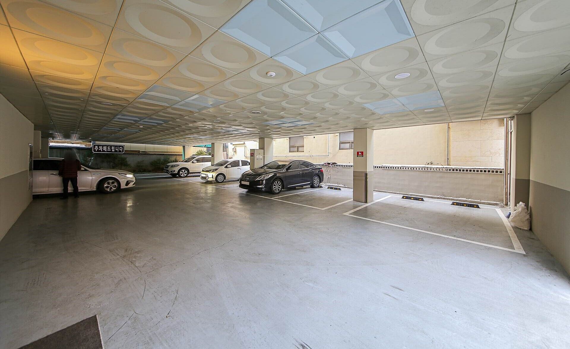 Un parking souterrain où sont garées plusieurs voitures, ainsi qu’un autobus, et où une personne se tient près d’une voiture.