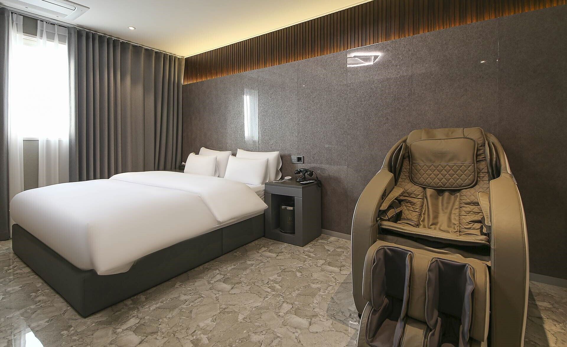 Een hotelkamer met een groot bed, een massagestoel en een nachtkastje met een lamp.