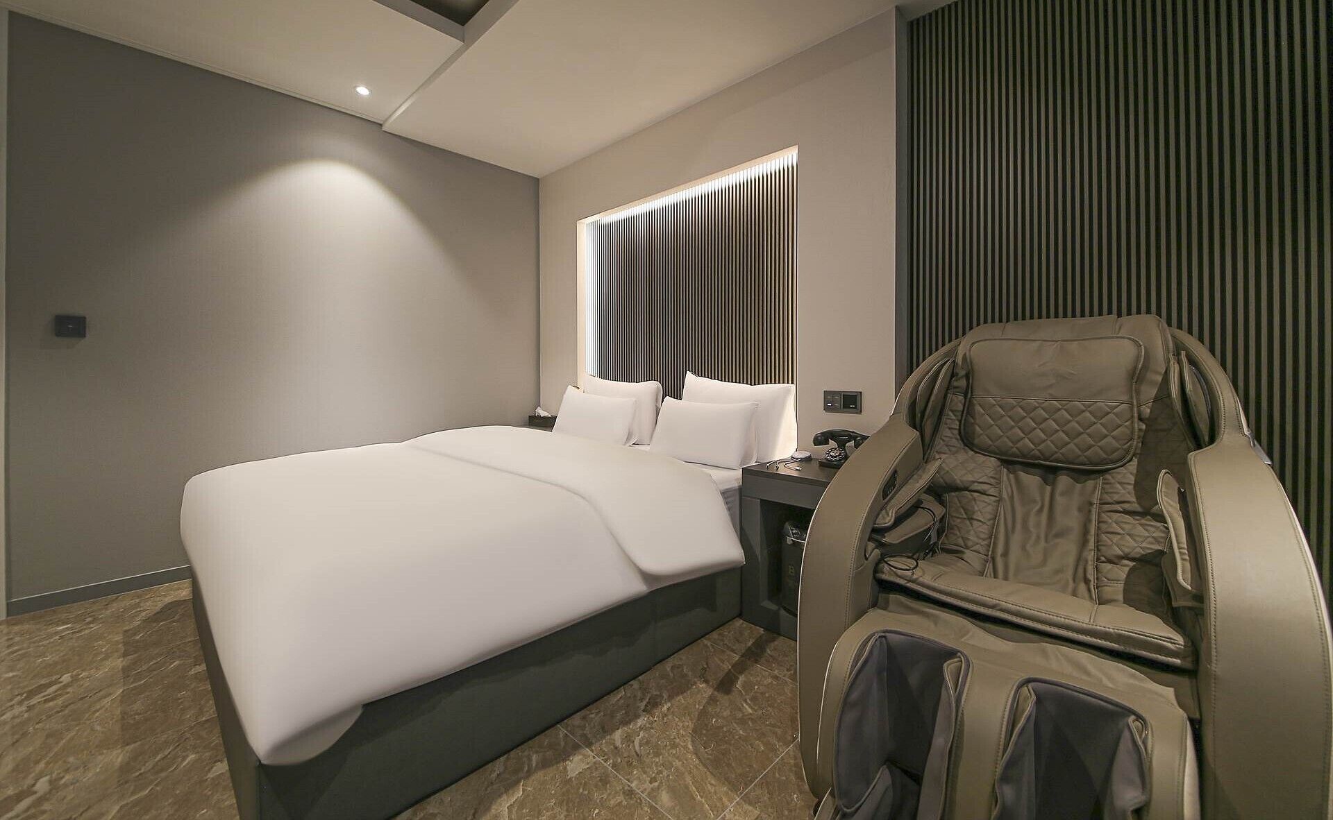 Une chambre d’hôtel moderne dotée d’un grand lit, d’un fauteuil massant et d’un panneau de commande.