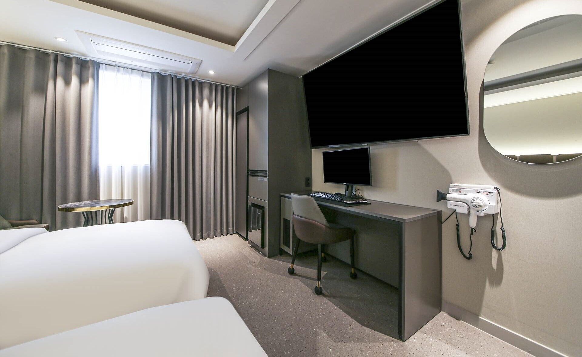 Una habitación de hotel con cama, escritorio, silla, televisor y secador de pelo.