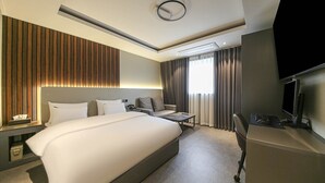 A modern hotel room with a large bed, a desk with a computer, a TV, and a window with curtains. - Chungju Browndot Cityhall (Chungju)