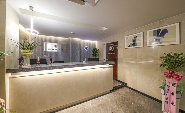 A hotel reception area with a modern design, featuring a reception desk, a wall-mounted sign, and framed artwork on the wall.