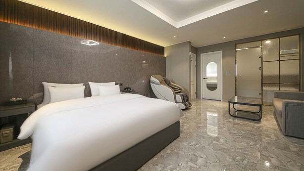 A modern hotel room with a large bed, a massage chair, and a glass-enclosed shower area. - Chungju Browndot Cityhall (Chungju)