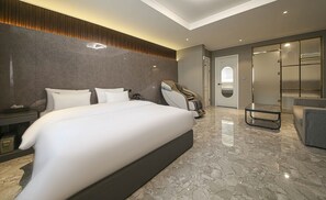 A modern hotel room with a large bed, a massage chair, and a glass-enclosed shower area.