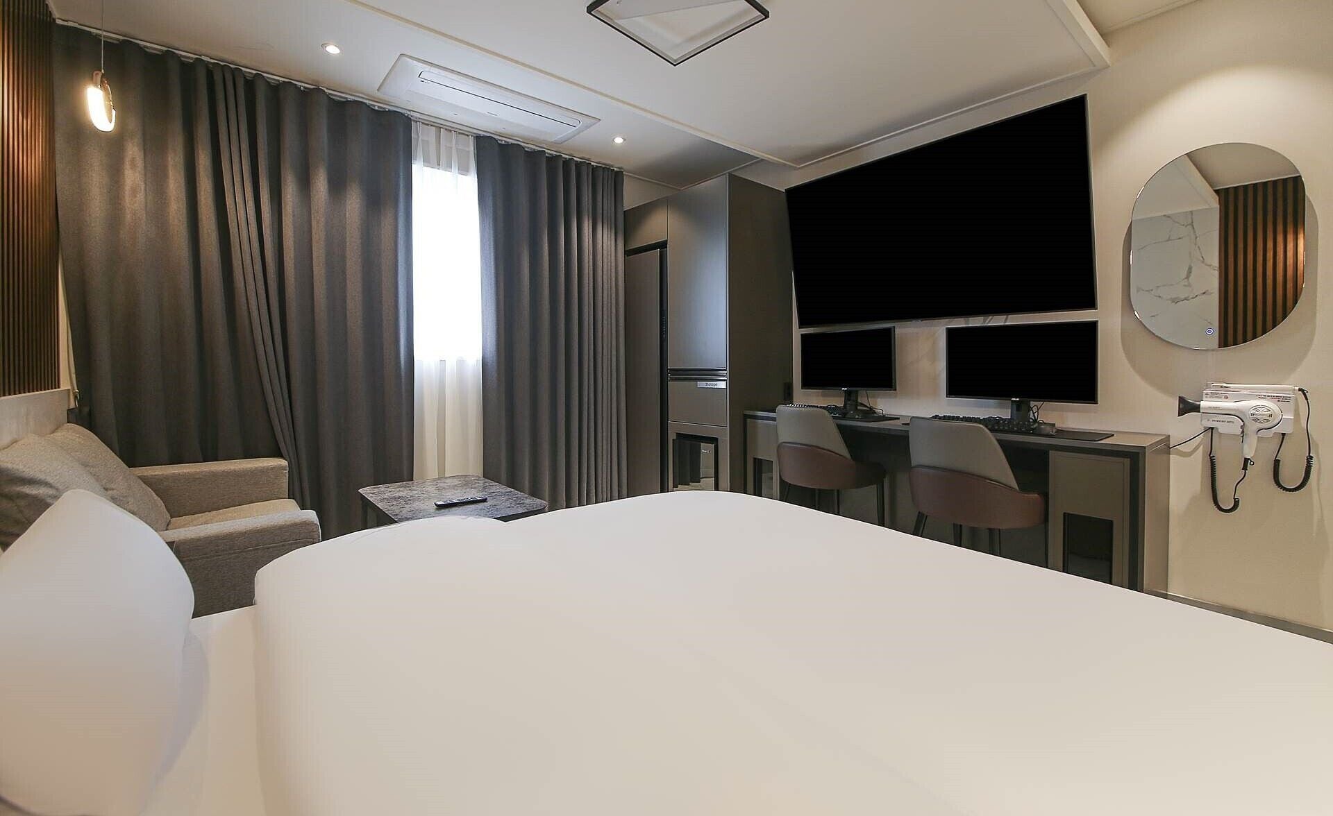A hotel room with a large bed, a desk with two monitors, a hairdryer, and a mirror on the wall.