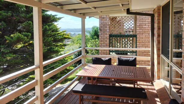 Un balcón con una mesa y sillas de madera, vistas a zonas verdes y un paisaje distante.