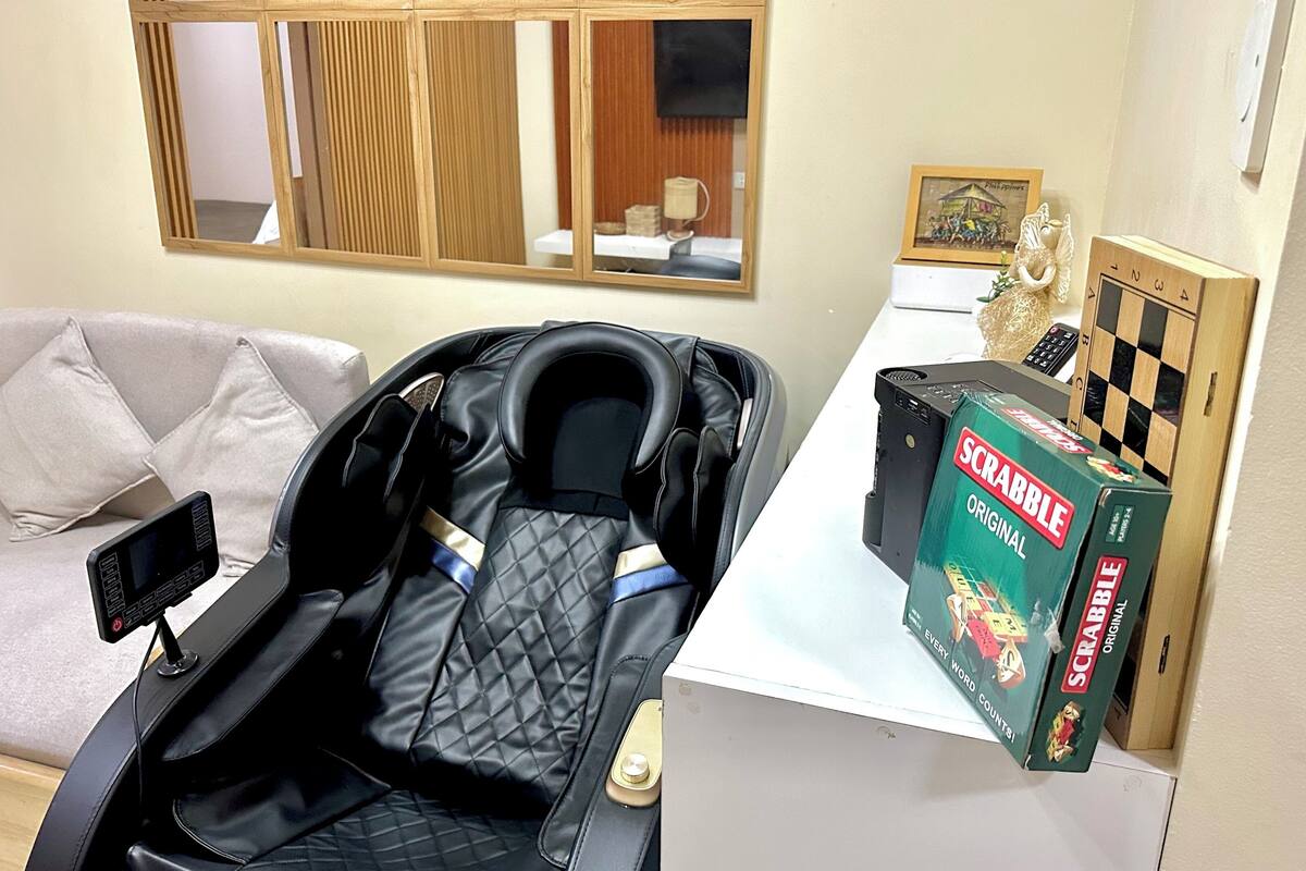 A room with a bed, a massage chair, a Scrabble box, and a small table with a lamp.