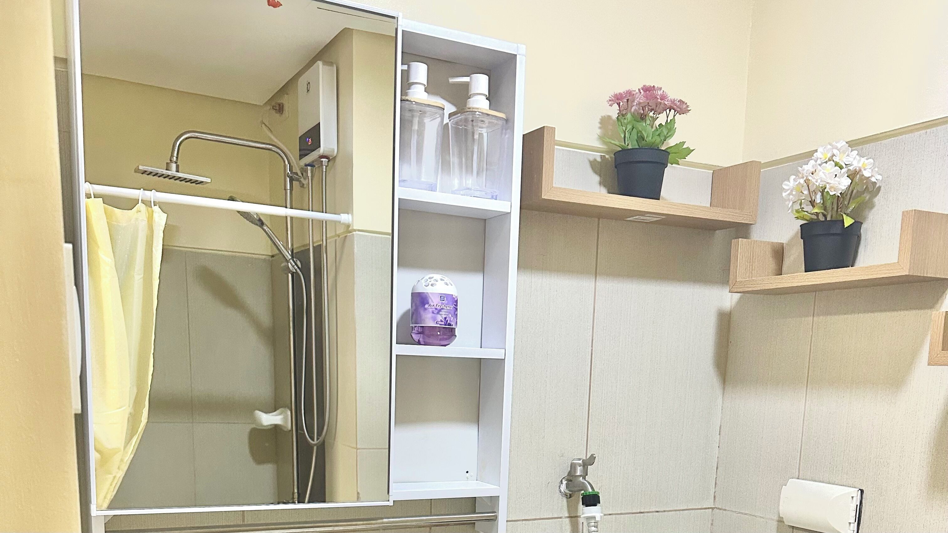 A bathroom with a shower, a toilet, and shelves with toiletries and a potted plant.