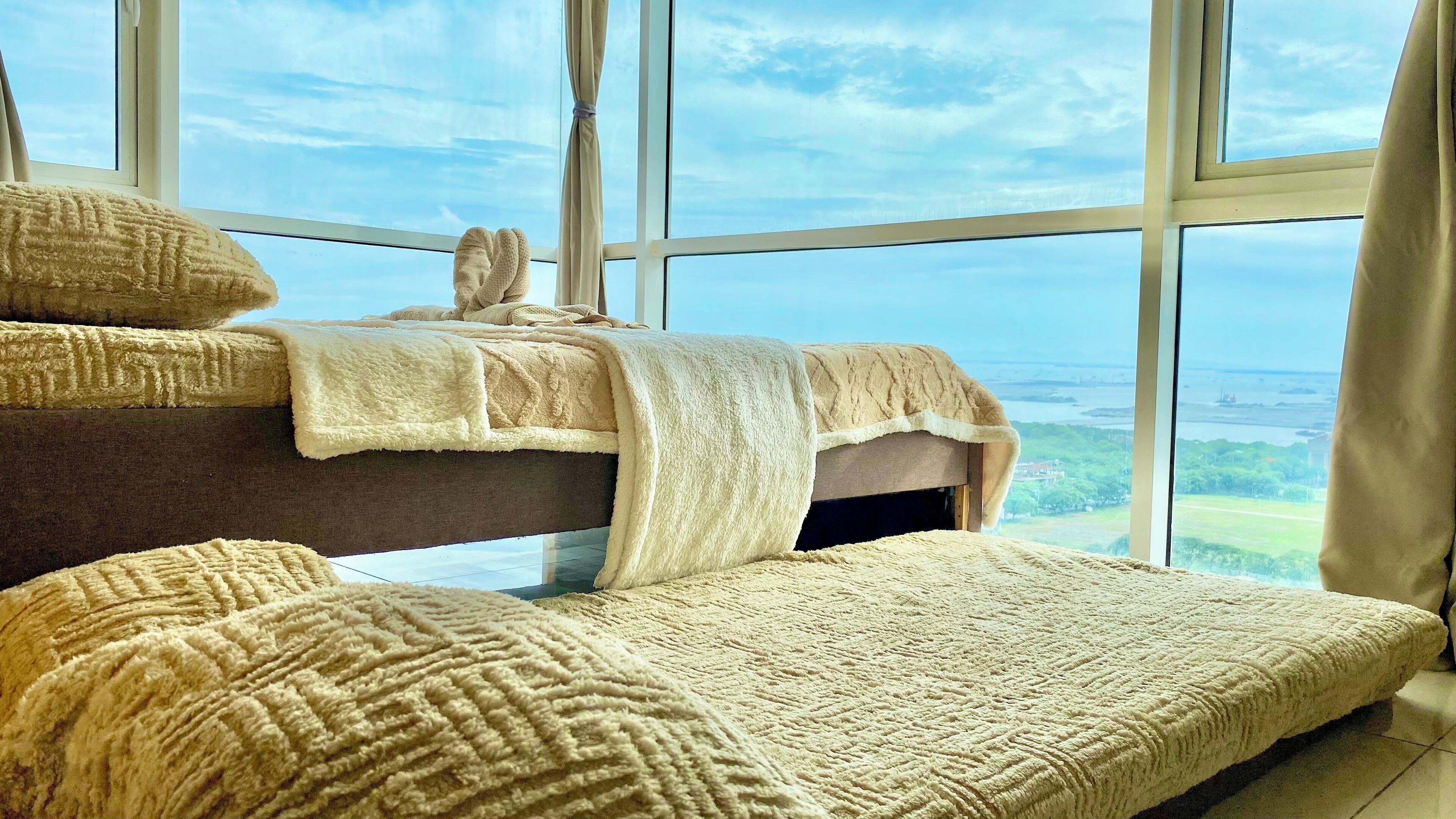 Ein Bett mit einer flauschigen weißen Decke und Kissen, ein Fenster mit Blick auf eine Landschaft und ein Vorhang.