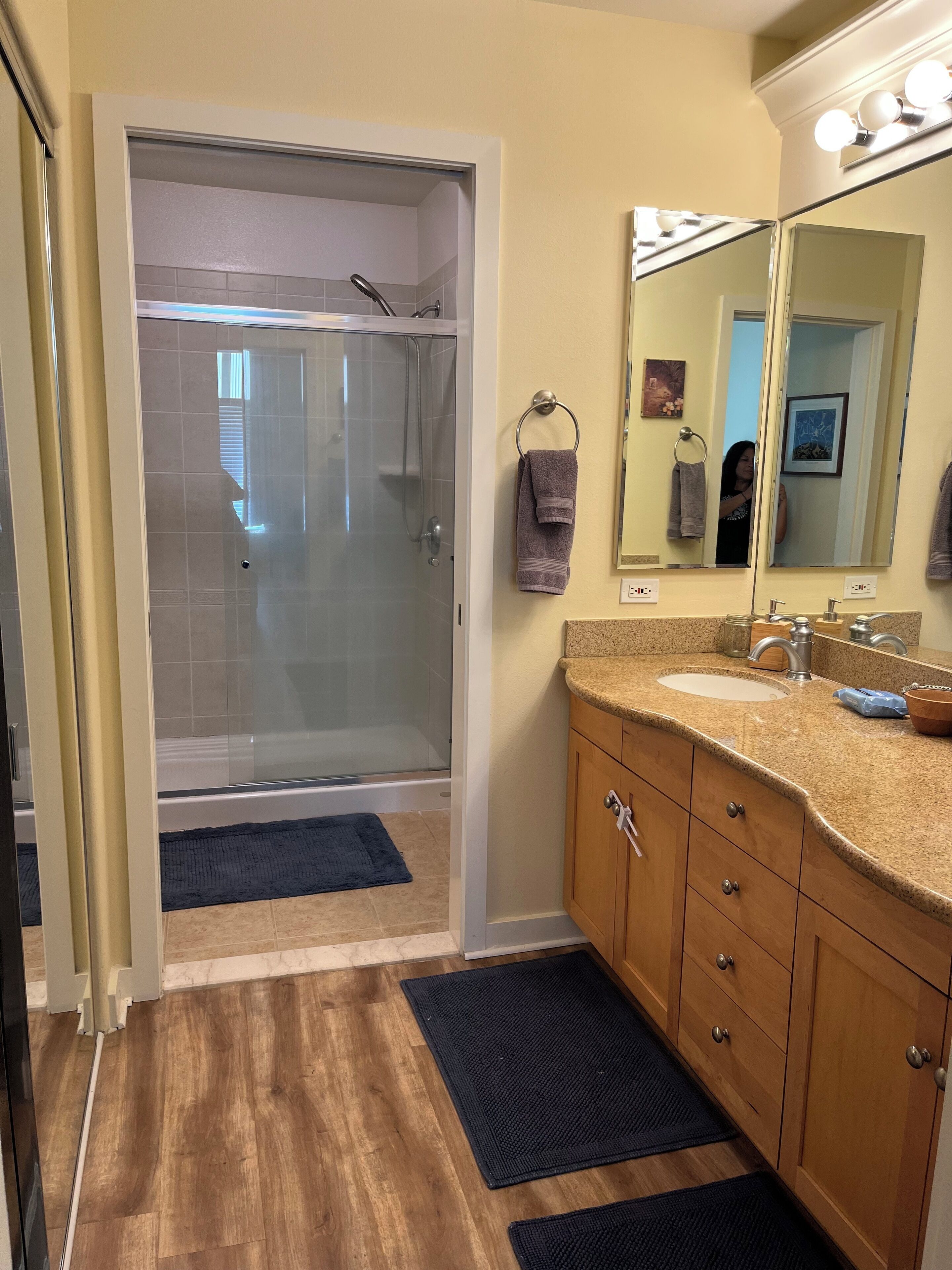 A bathroom with a glass-enclosed shower, wooden vanity, and a large mirror with lights.