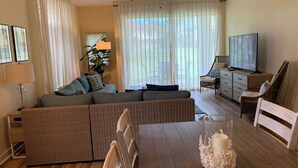 A living room with a sofa, dining table, chairs, a TV, and a ceiling fan.
