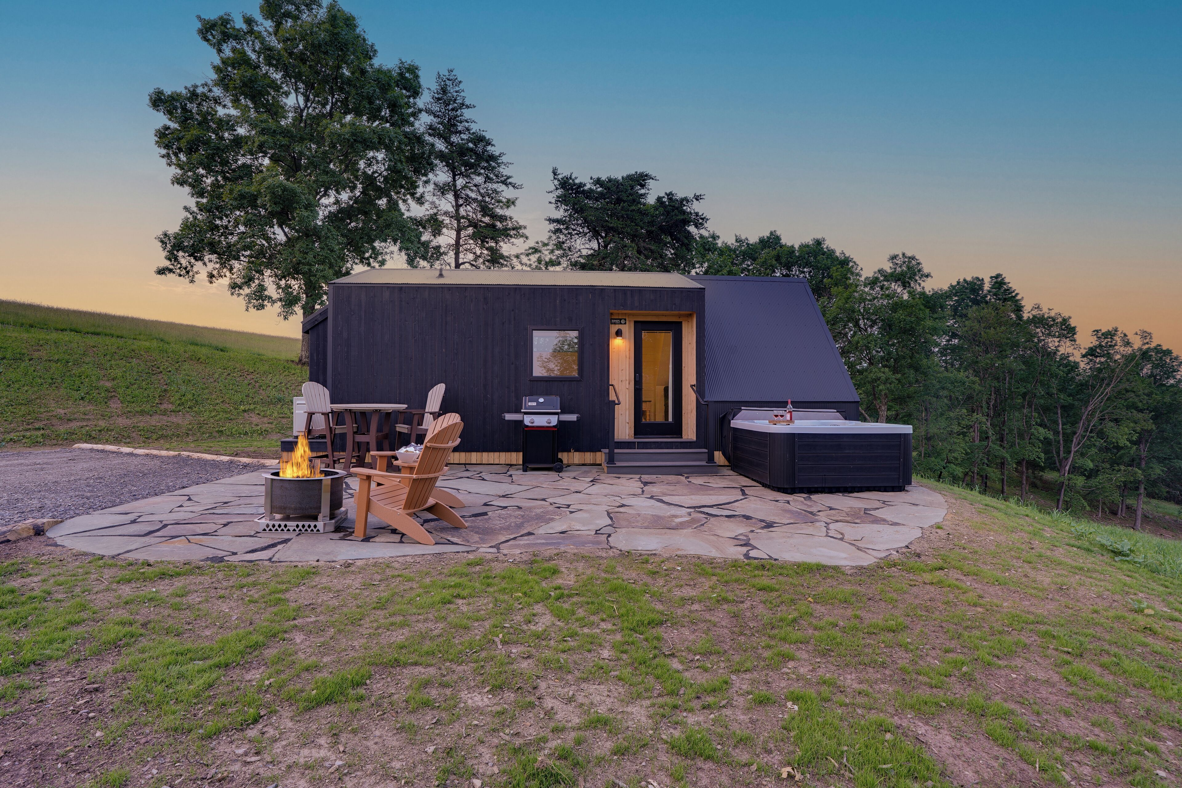 A modern cabin with a stone patio, outdoor seating, and a fire pit.