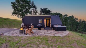 A modern cabin with a stone patio, outdoor seating, and a fire pit.