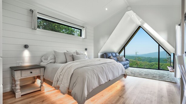 Ein Schlafzimmer mit einem großen Bett, einem Nachttisch, einem Fenster und Blick ins Freie.