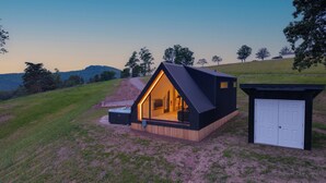 Eine moderne, dreieckige Hütte mit offenem Innenraum, Whirlpool und kleiner Lagerhütte.
