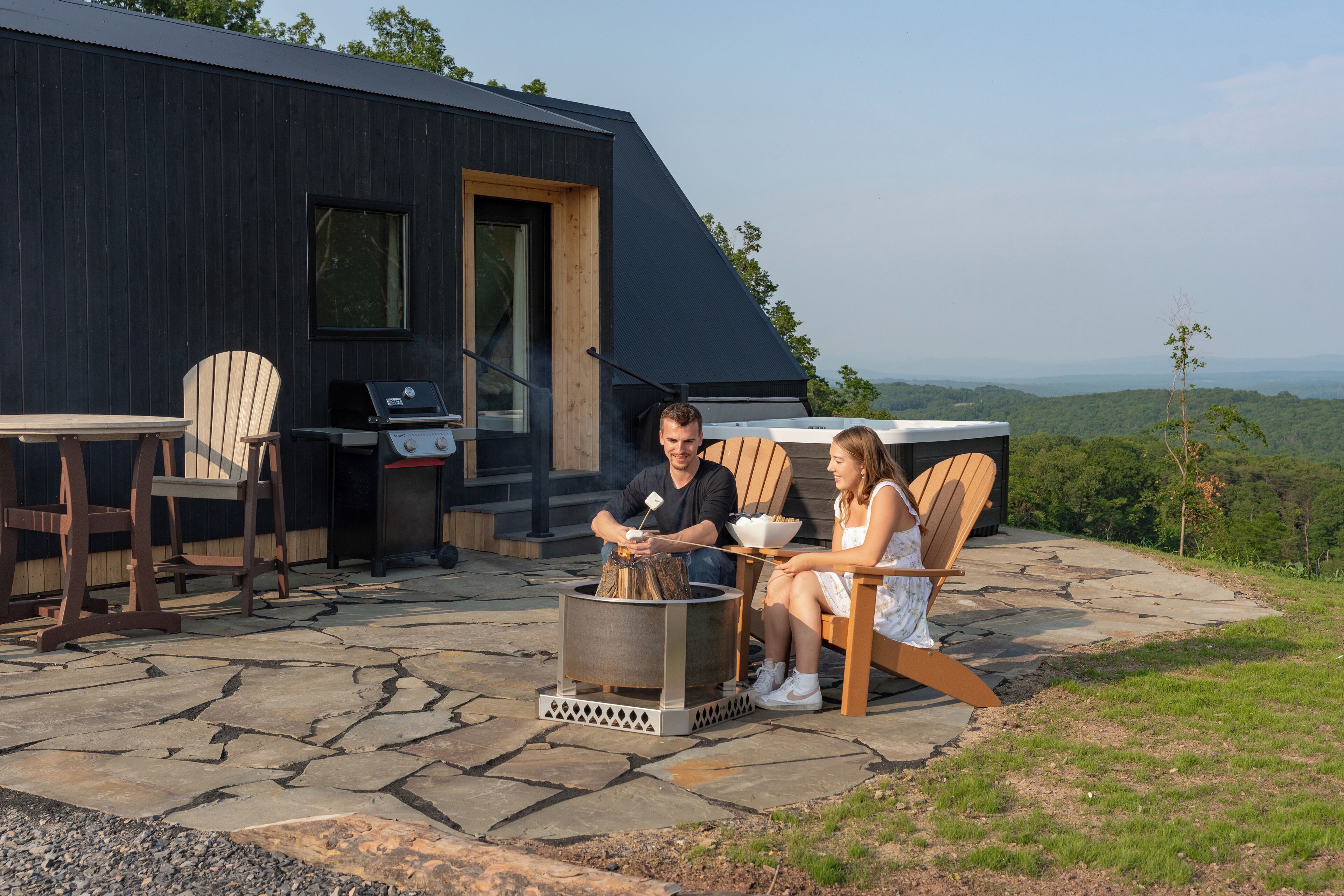 Un espacio moderno para sentarse al aire libre, con un patio de piedra, un brasero y vistas del paisaje circundante.