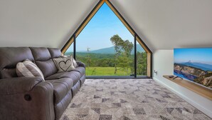 Ein modernes Wohnzimmer mit einer braunen Ledersofa, einem gemusterten Teppich und einem großen Fenster mit herrlichem Blick auf eine Berglandschaft.