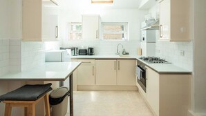 A compact kitchen with white cabinets, a gas stove, a sink, and a window. - Super 2BD Maisonette in Queens Park, Maida Vale (London)