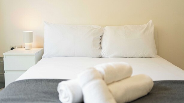 A neatly made bed with white linens and two rolled towels on a gray blanket. - Super 2BD Maisonette in Queens Park, Maida Vale (London)