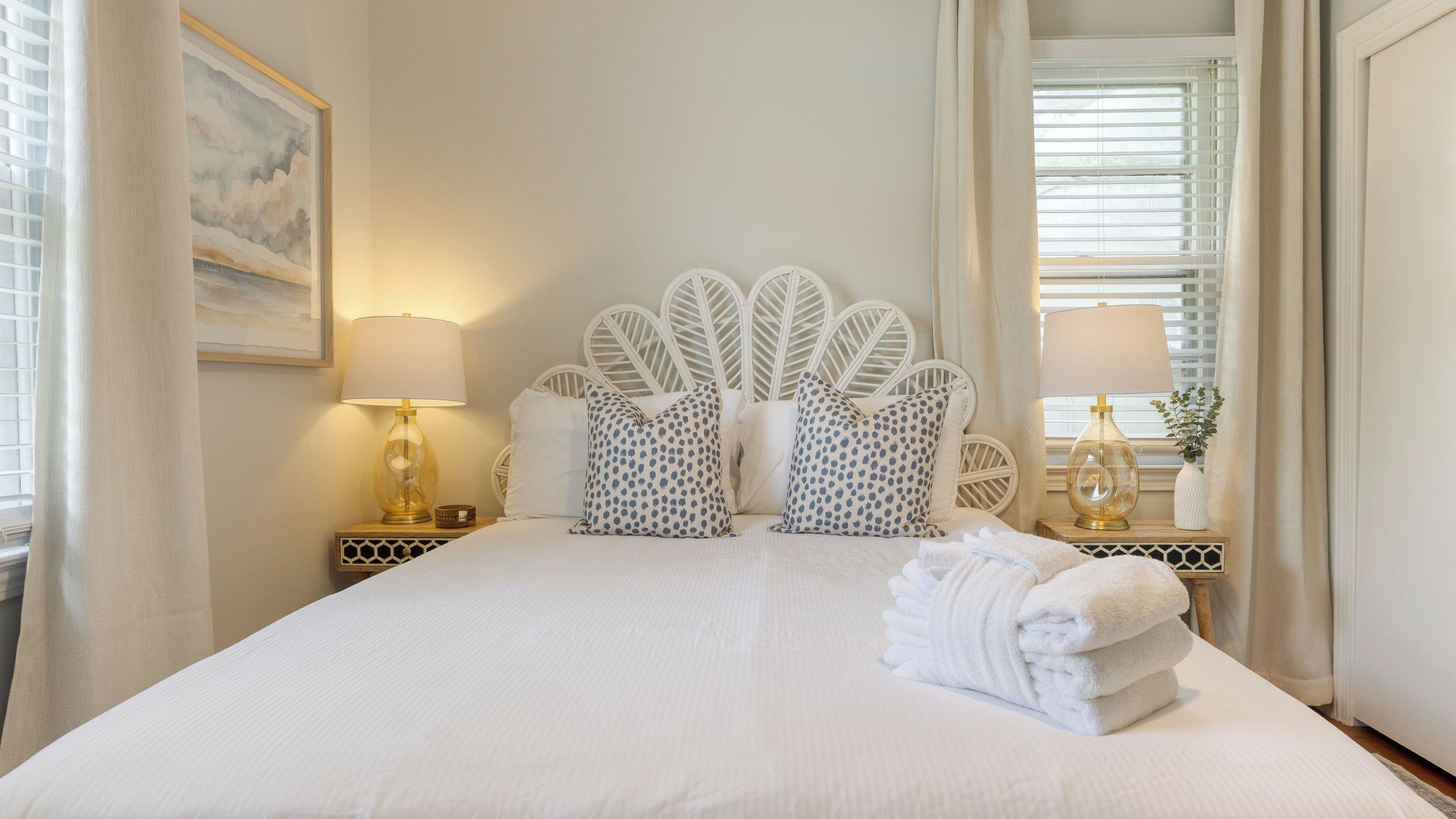 A neatly made bed with white linens, two patterned pillows, and a folded towel on a wooden nightstand.