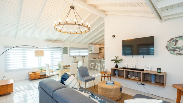 A modern living room with a grey sofa, a round ottoman, and a TV mounted on the wall.