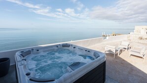 A hot tub with a view of the sea, outdoor seating, and a stone wall.