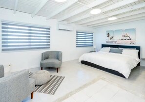 A modern bedroom with a large bed, two windows with blinds, a chair, and a painting on the wall.