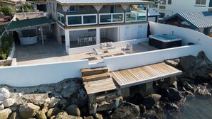 A two-story beachfront property with a covered patio, outdoor seating, and a hot tub.