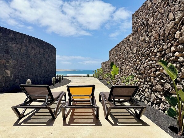Un coin détente avec trois chaises et une table, offrant une vue sur la plage et l’océan.