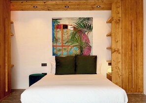Une chambre à coucher avec un grand lit, une tête de lit en bois, une peinture murale représentant une végétation tropicale et une table de chevet avec une lampe.
