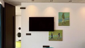 Een moderne woonkamer met een flatscreen televisie aan de muur, blauwe poefs en een houten salontafel.